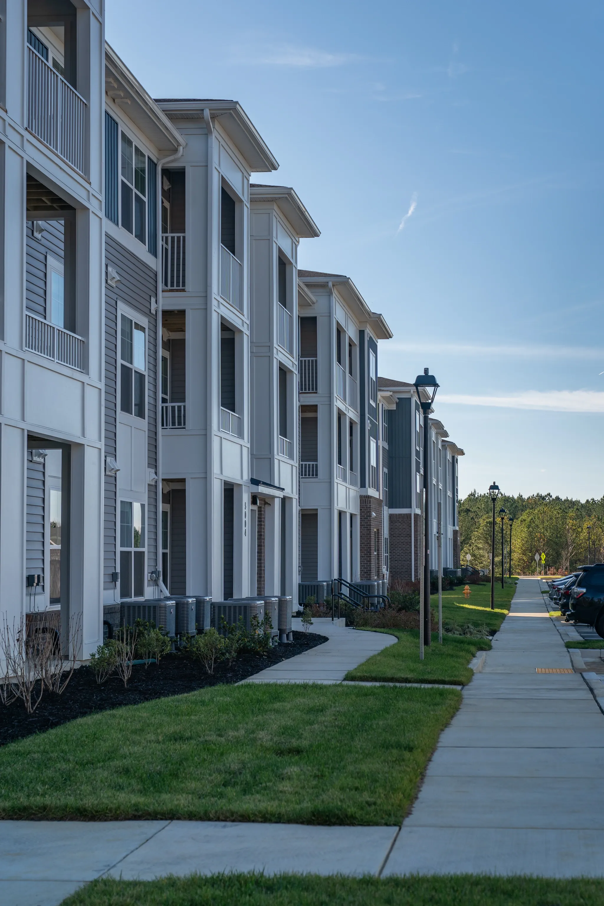 Exterior view of a modern apartment building with balconies and a sidewalk.