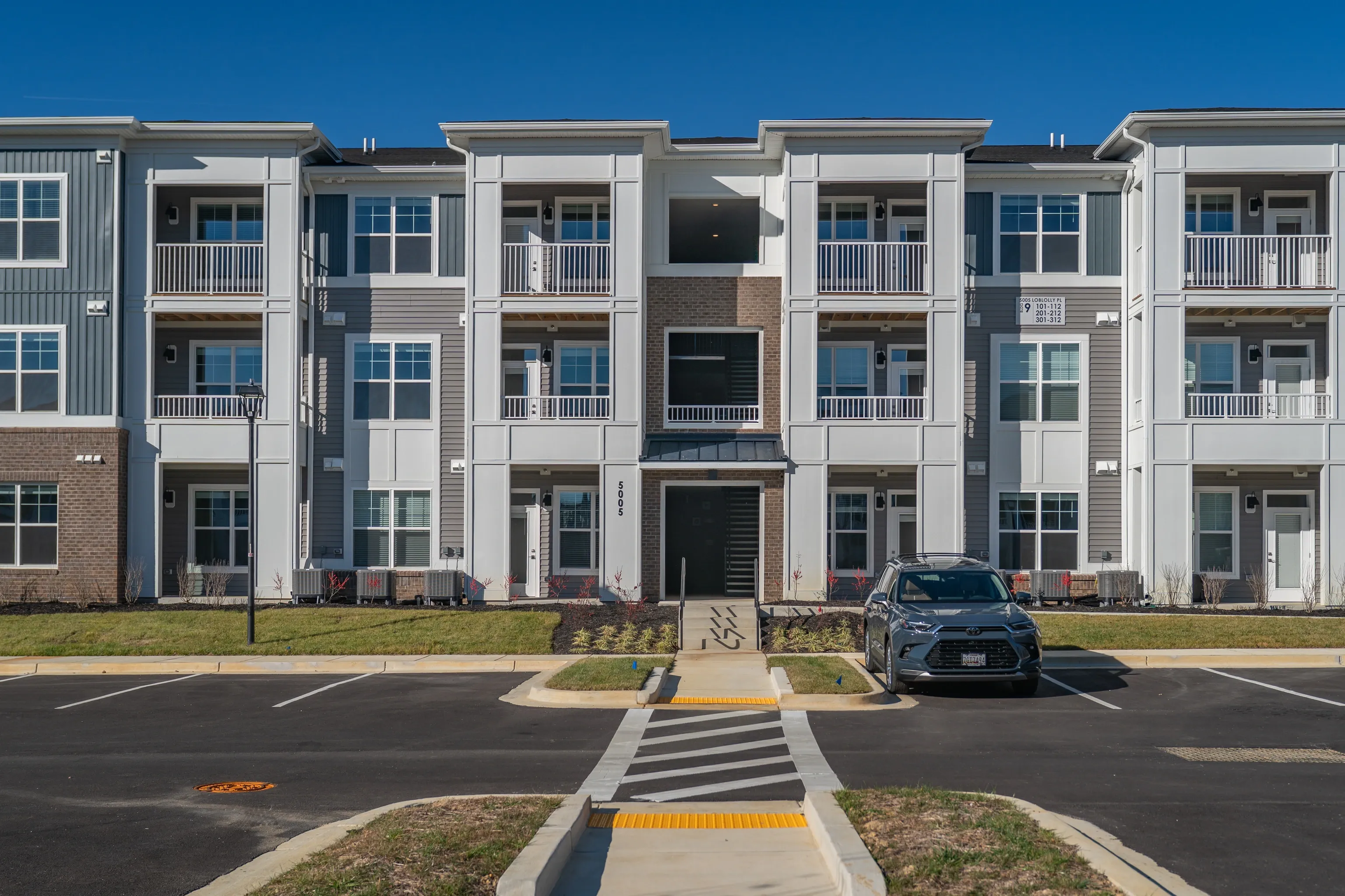 Exterior view of apartment building with balconies and parking lot.