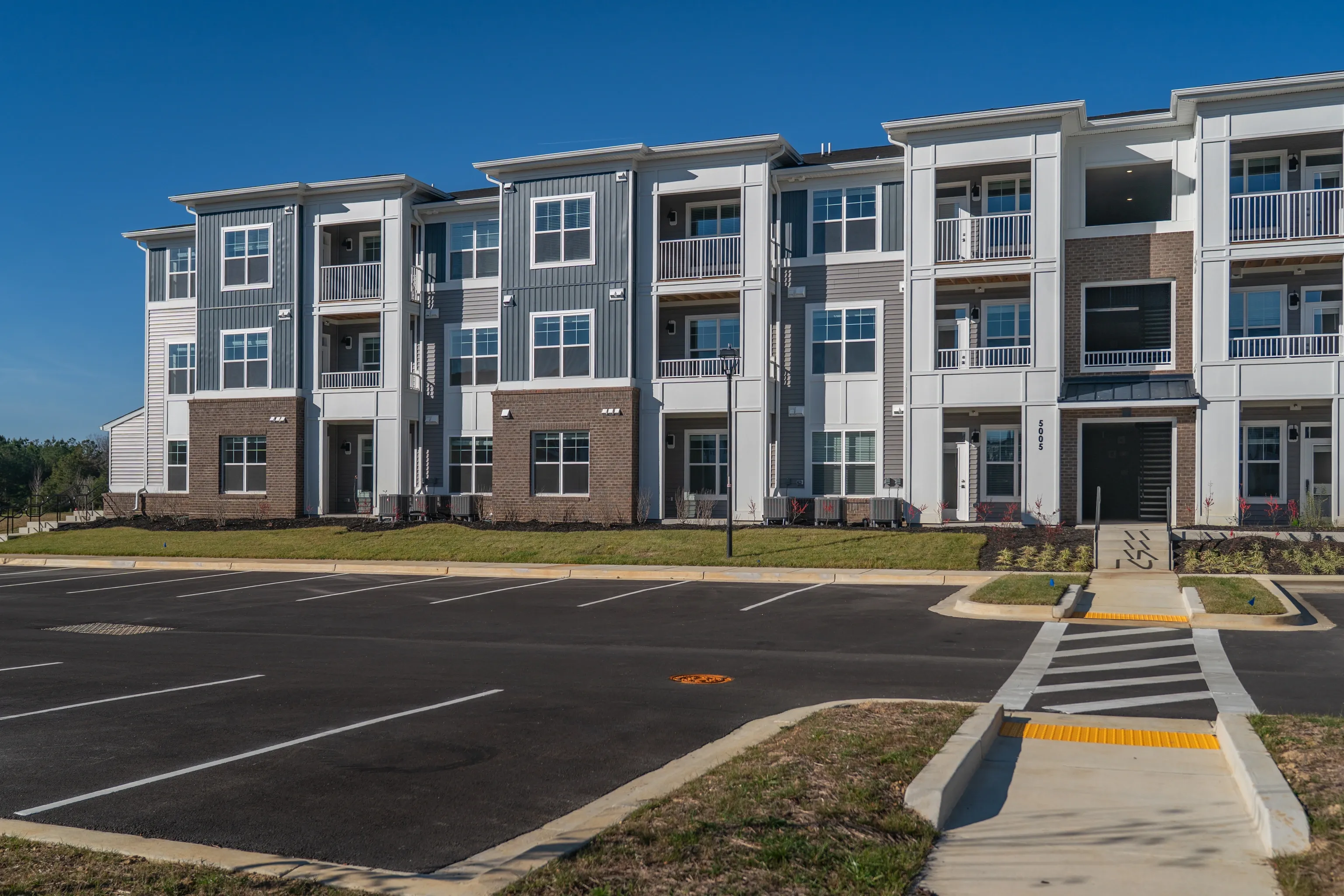 Exterior view of a modern apartment building with a parking lot in the foreground.