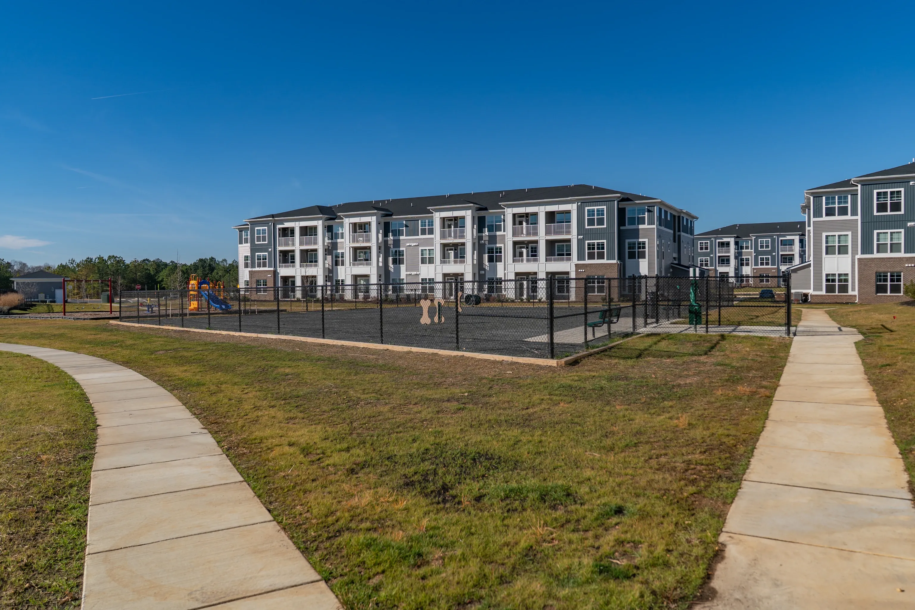 Apartment buildings with a fenced dog park and playground in the foreground.