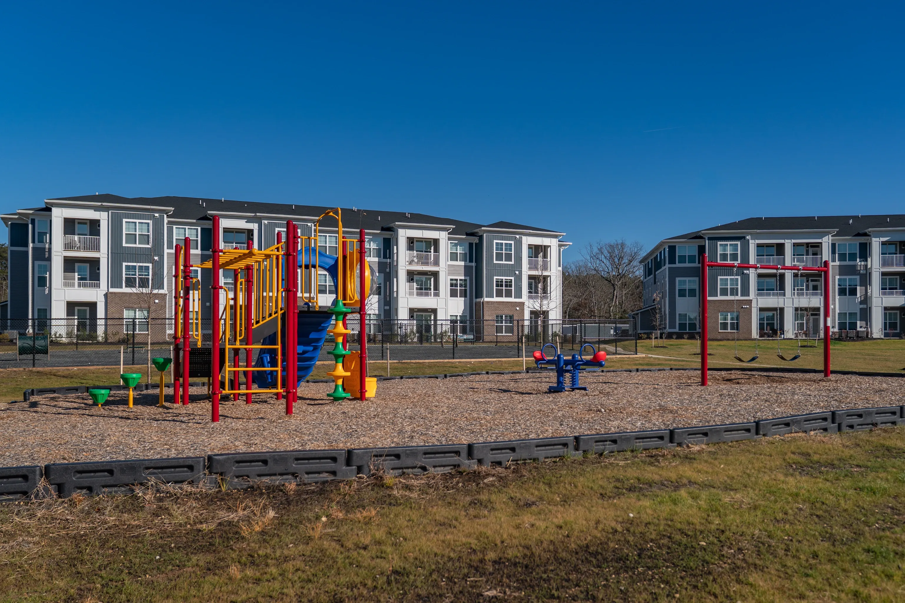 Playground with slides and swings in front of apartment buildings.