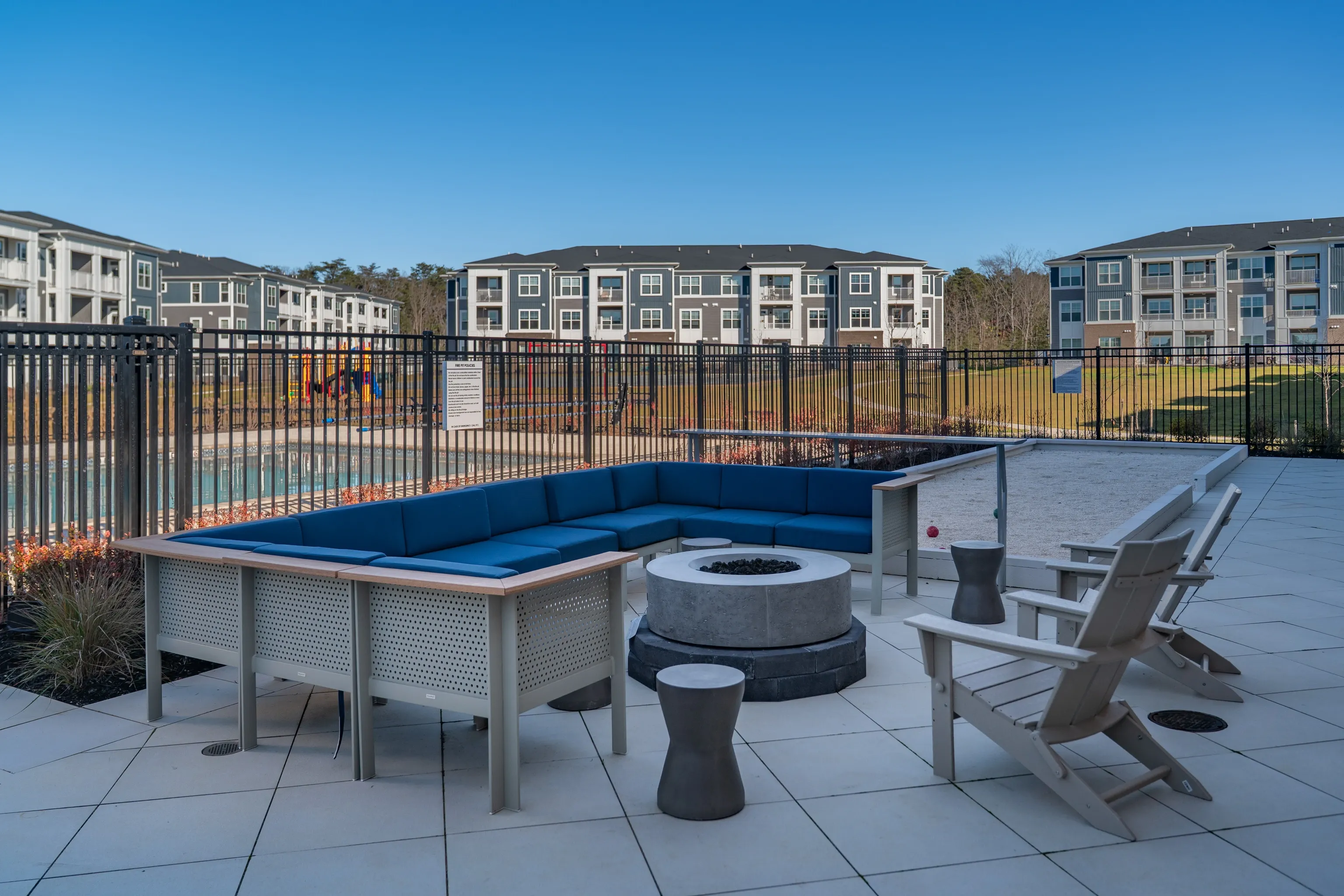 Outdoor seating area with fire pit and bocce ball court overlooking apartments and pool.
