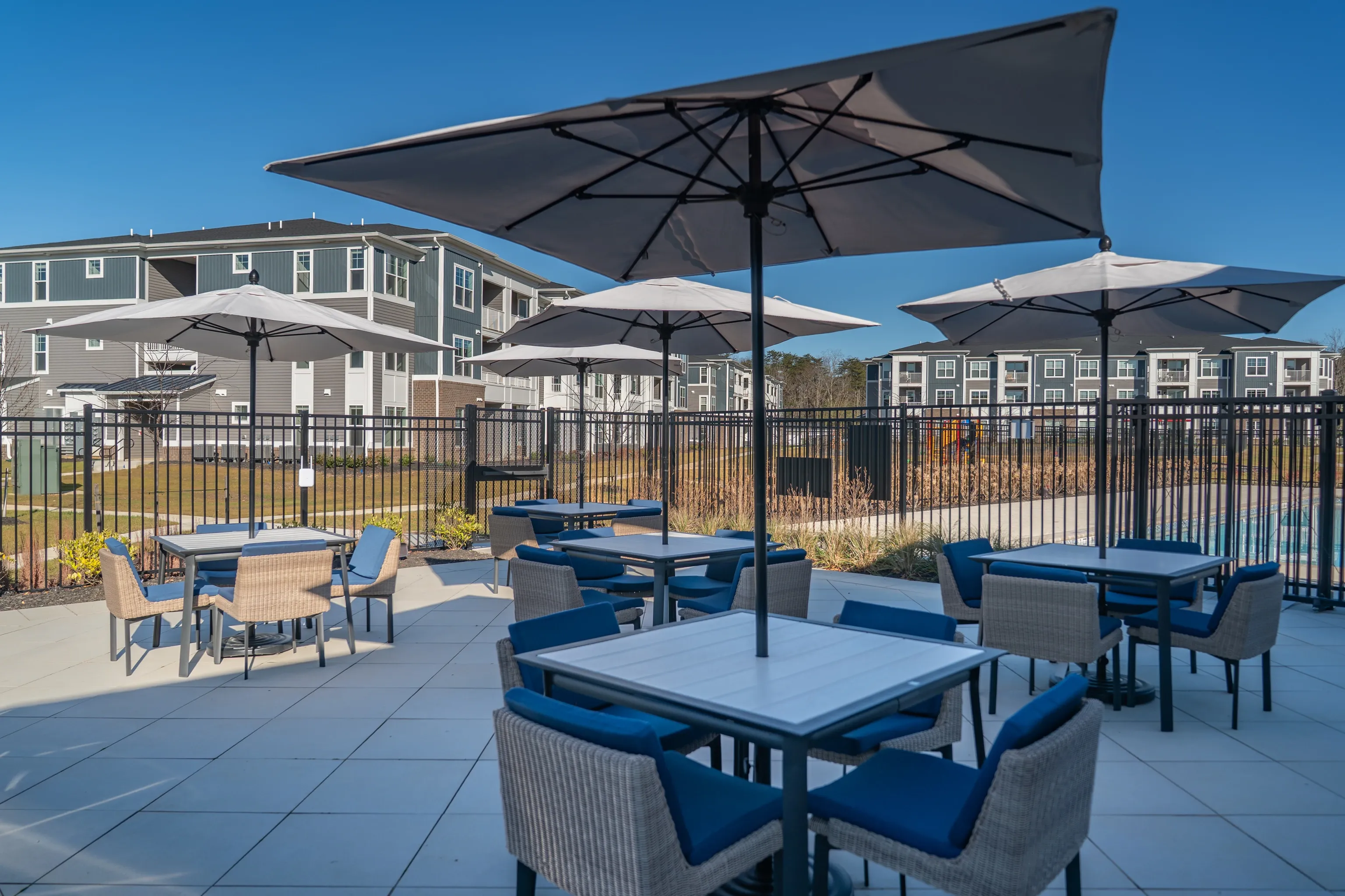 Outdoor seating area with tables and umbrellas in front of apartment buildings.