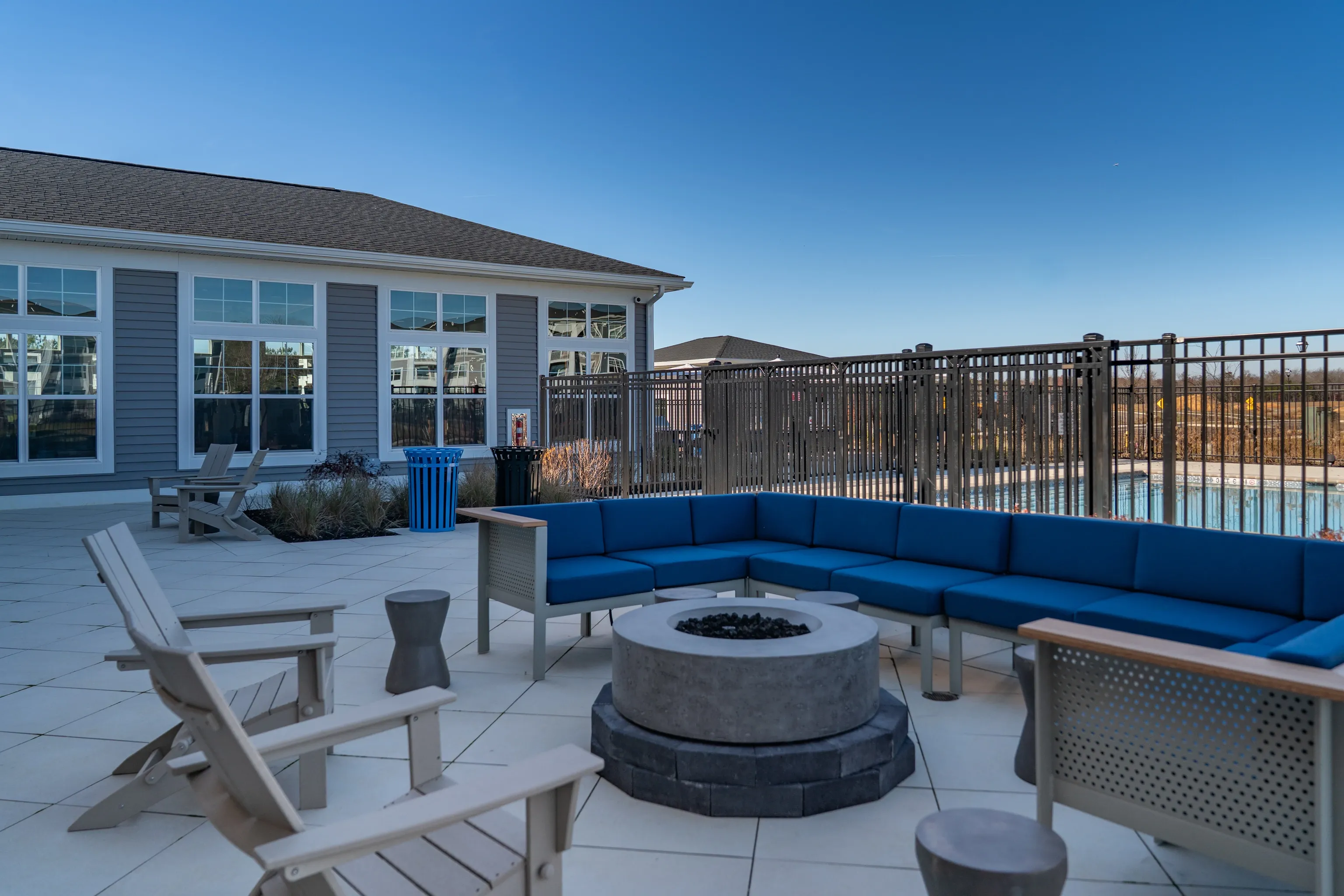 Outdoor seating area with a fire pit and lounge chairs next to a swimming pool.