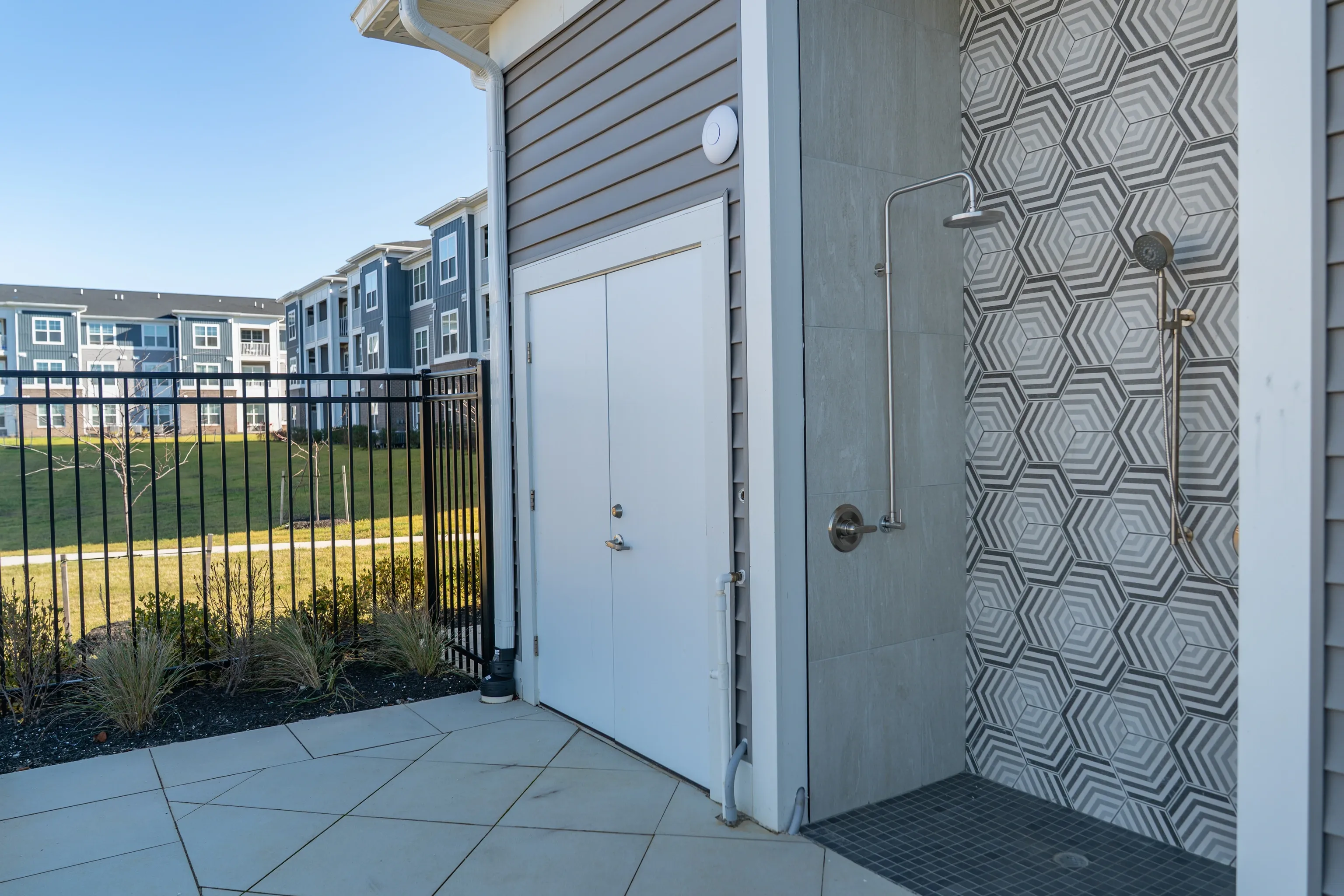 Outdoor shower area with patterned tile, adjacent to building with double doors.