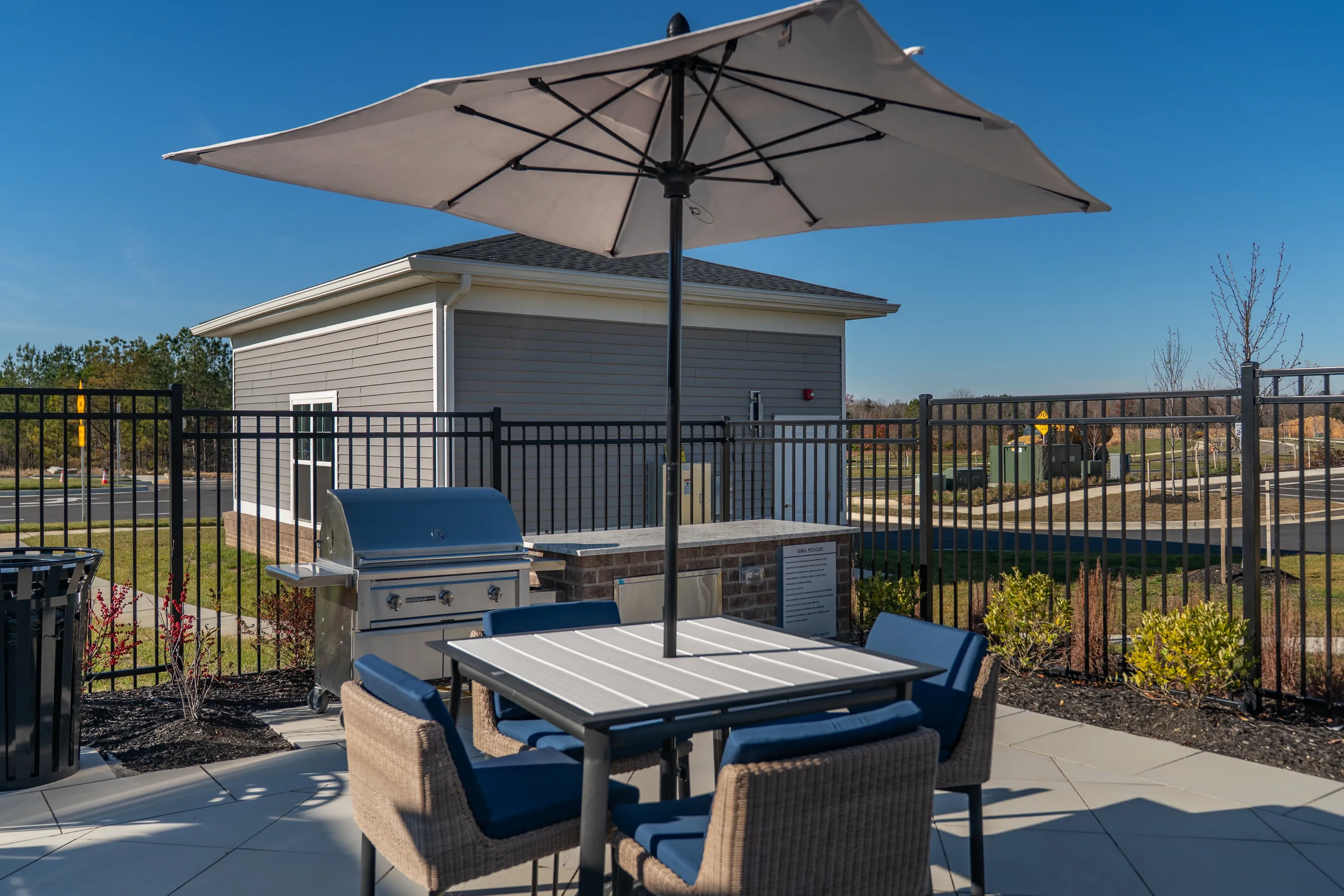 Outdoor grilling area with table, chairs, and umbrella.