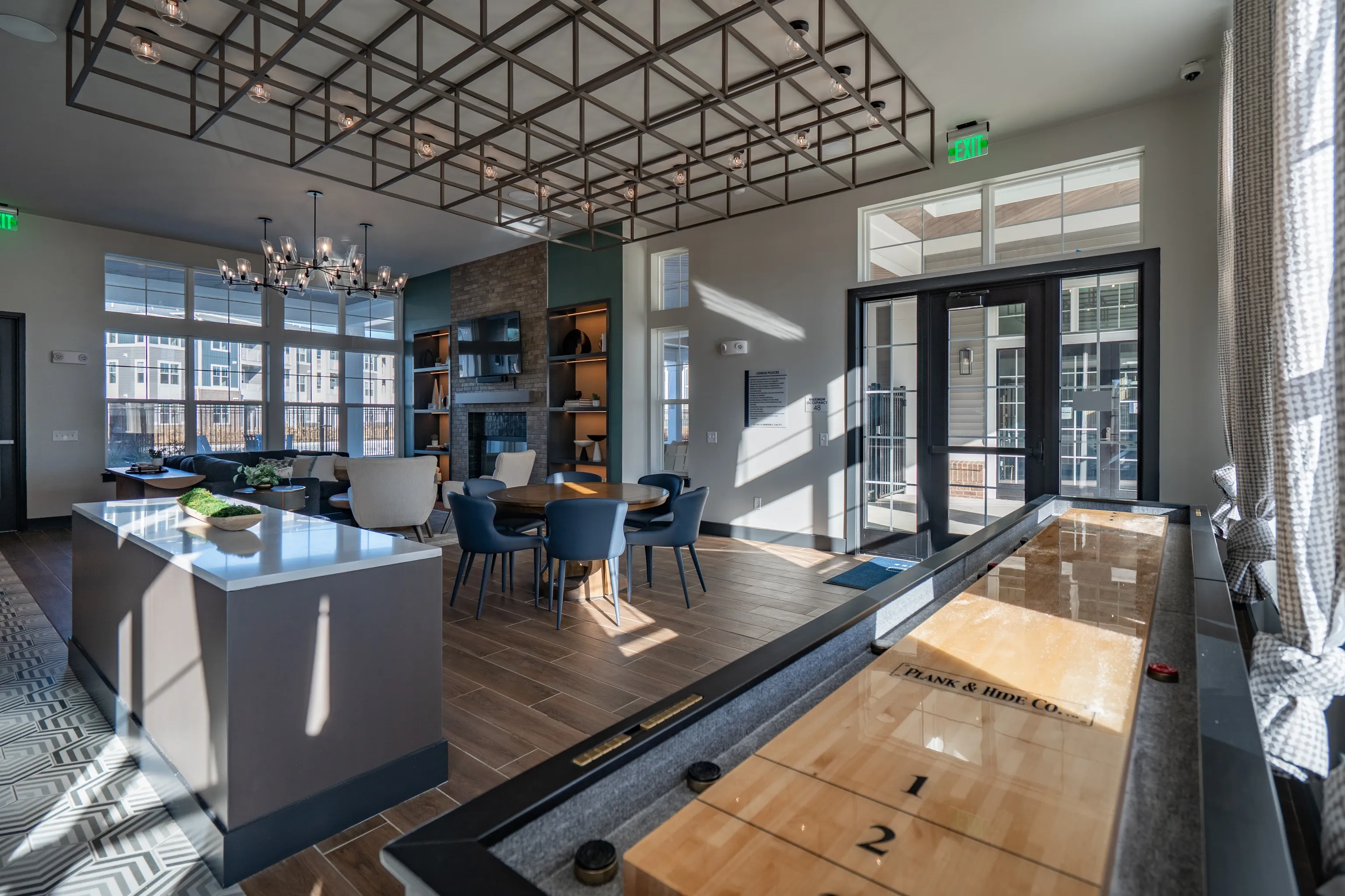 Community lounge area with shuffleboard table, fireplace, seating, and large windows.