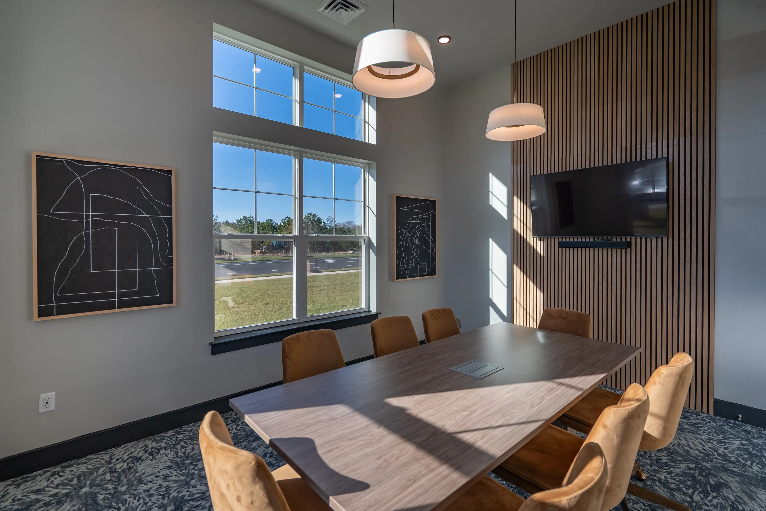 Modern conference room with a large wooden table, comfortable chairs, and a TV.