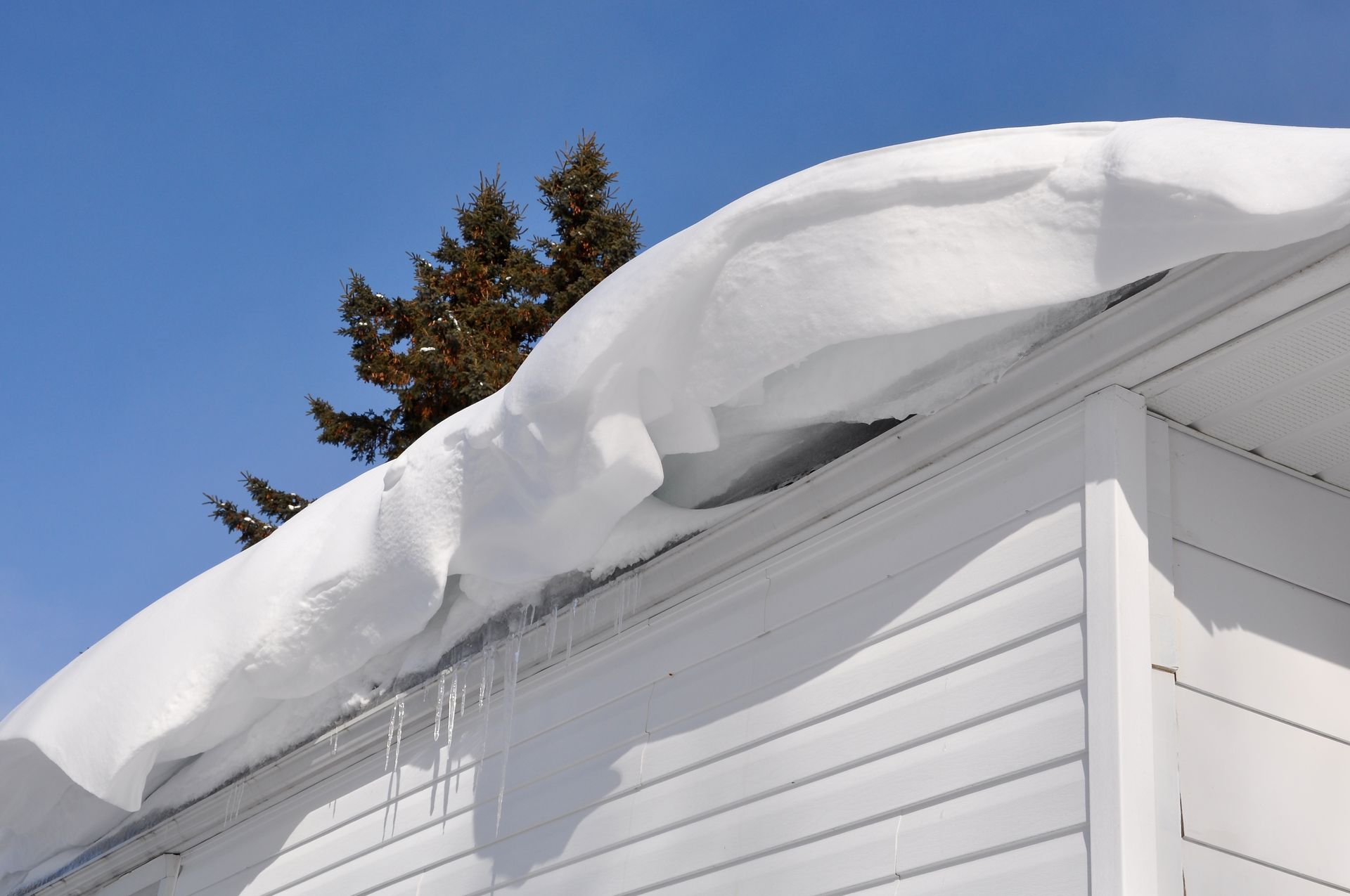 Deep snow overhanging a roof edge with icicles forming along the gutter line.