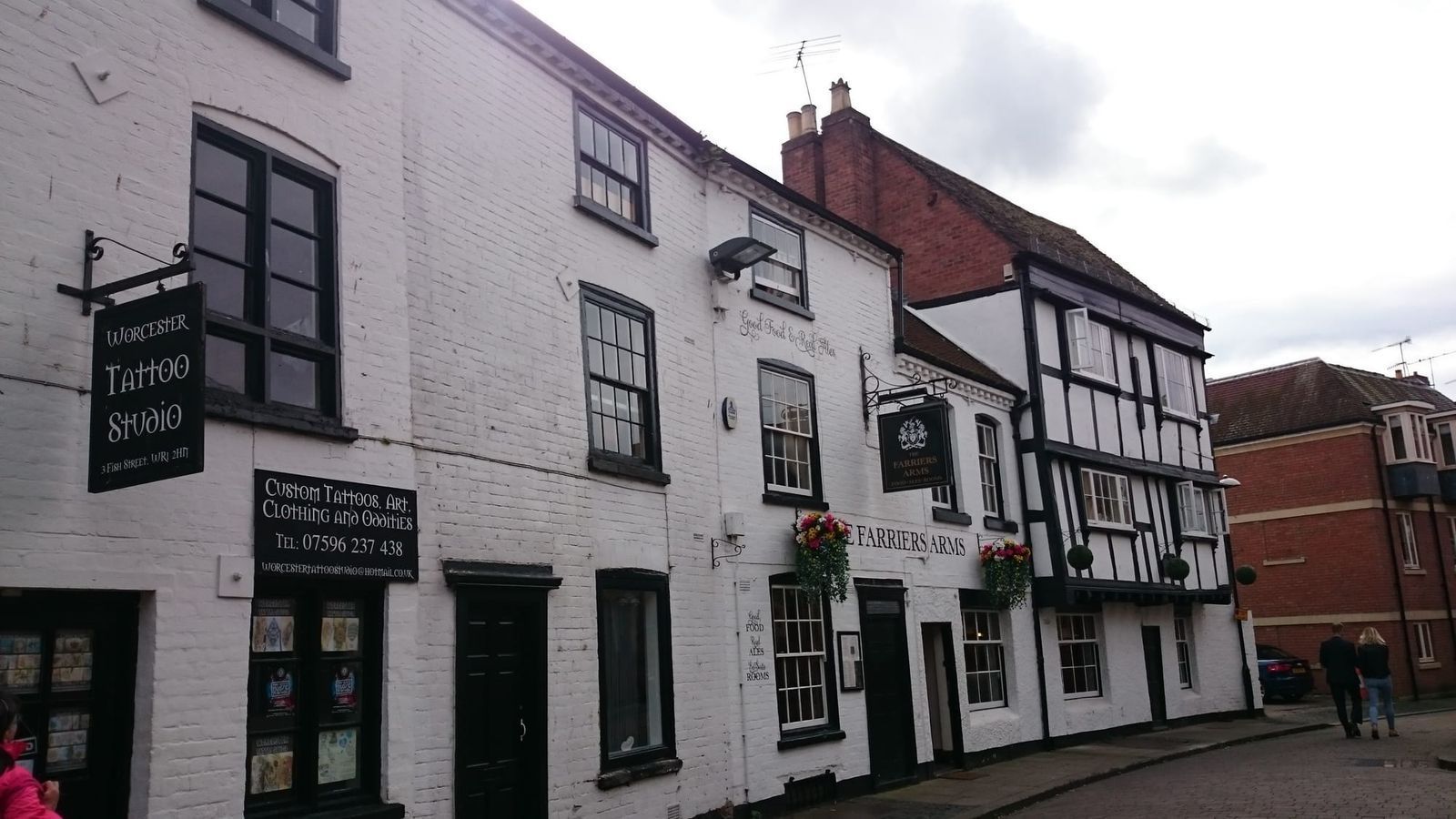 Row of white and black timber-framed pub buildings on a street, under an overcast sky