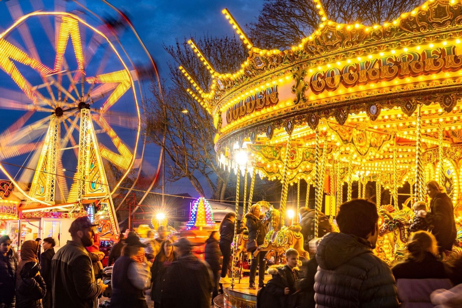 Ferris wheel and glowing carousel at a crowded night fair with bright lights