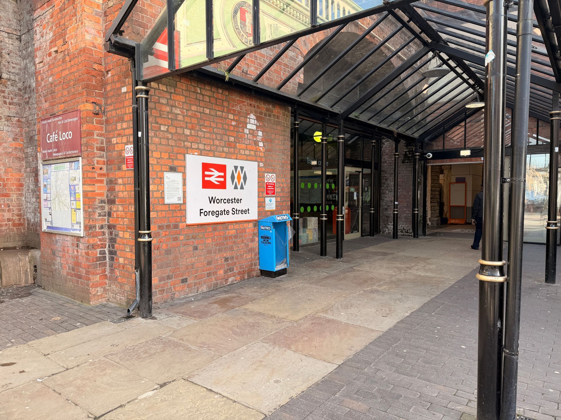 Brick building entrance with glass canopy, blue bin, and signs on the wall
