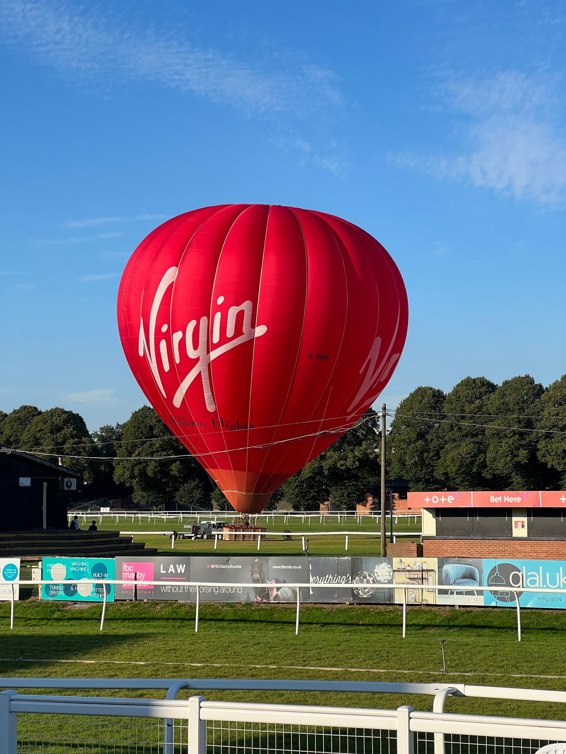 Red Virgin hot air balloon near a racetrack under a blue sky
