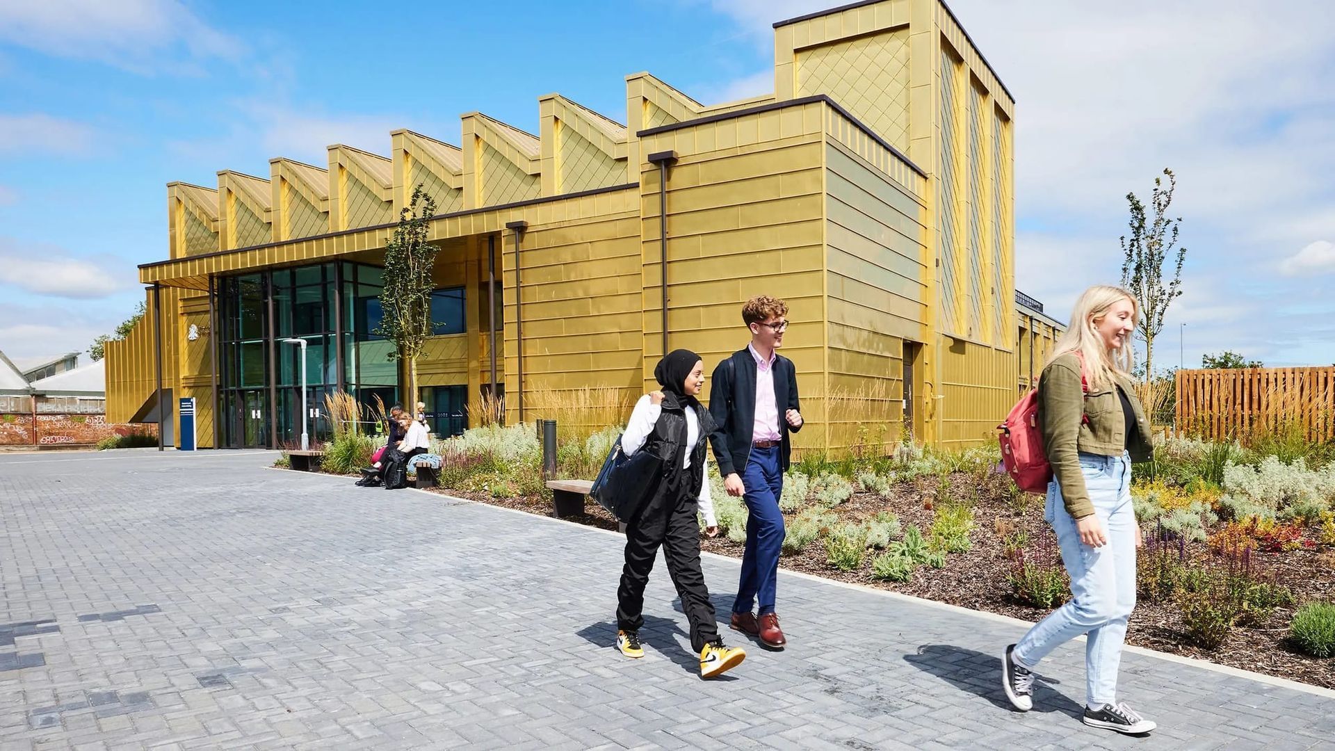 People walking past a modern yellow building with glass windows on a sunny day