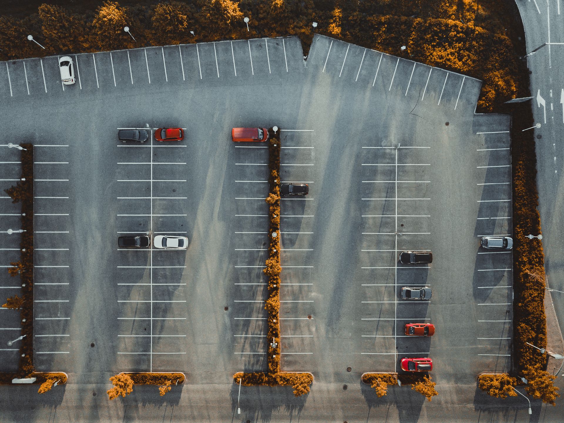 Aerial view of a mostly empty parking lot with a few parked cars and autumn trees along the edges