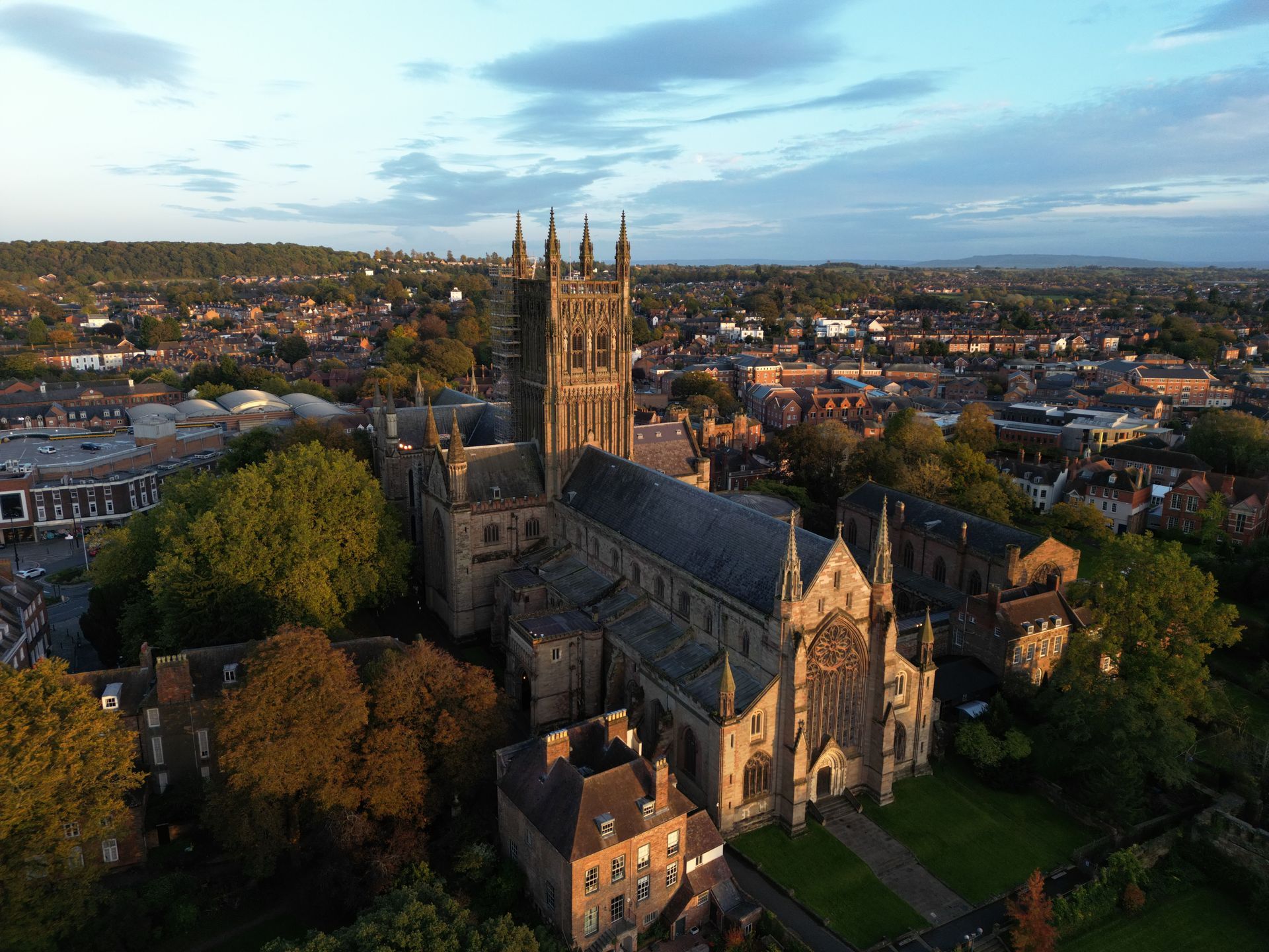 Aerial view of a historic stone cathedral amid autumn trees and a town at sunset.