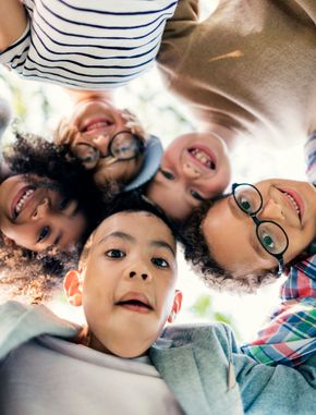 A diverse group of smiling children looking down into the camera from a circle, heads close together.