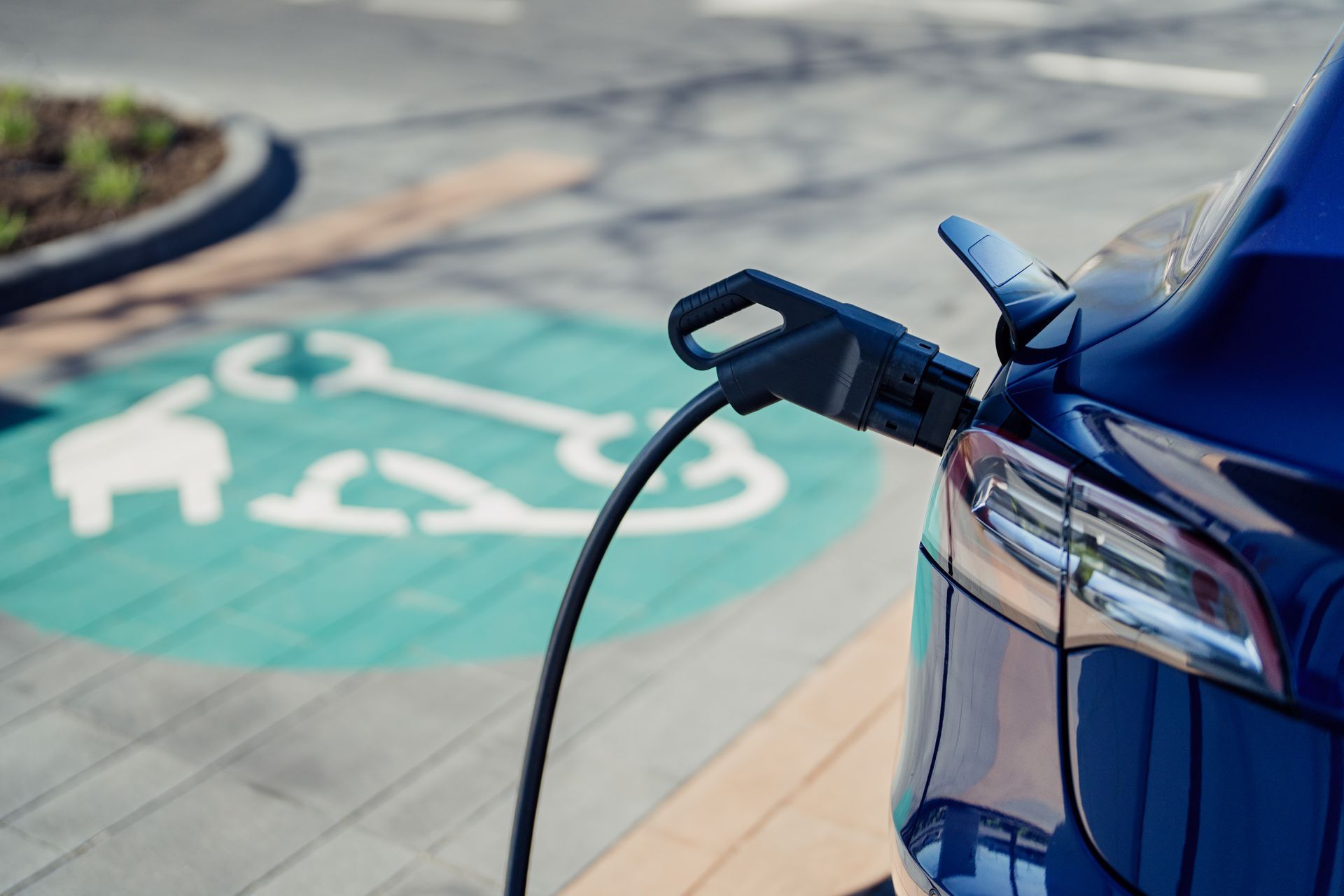 Blue electric car plugged into a charging station in a parking space marked with EV symbol