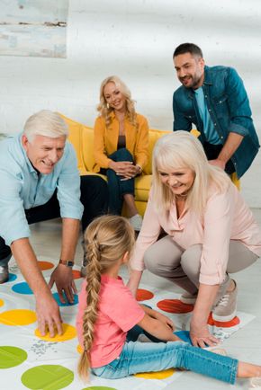 A multi-generational family playing a colorful floor game together in a bright, casual living room.