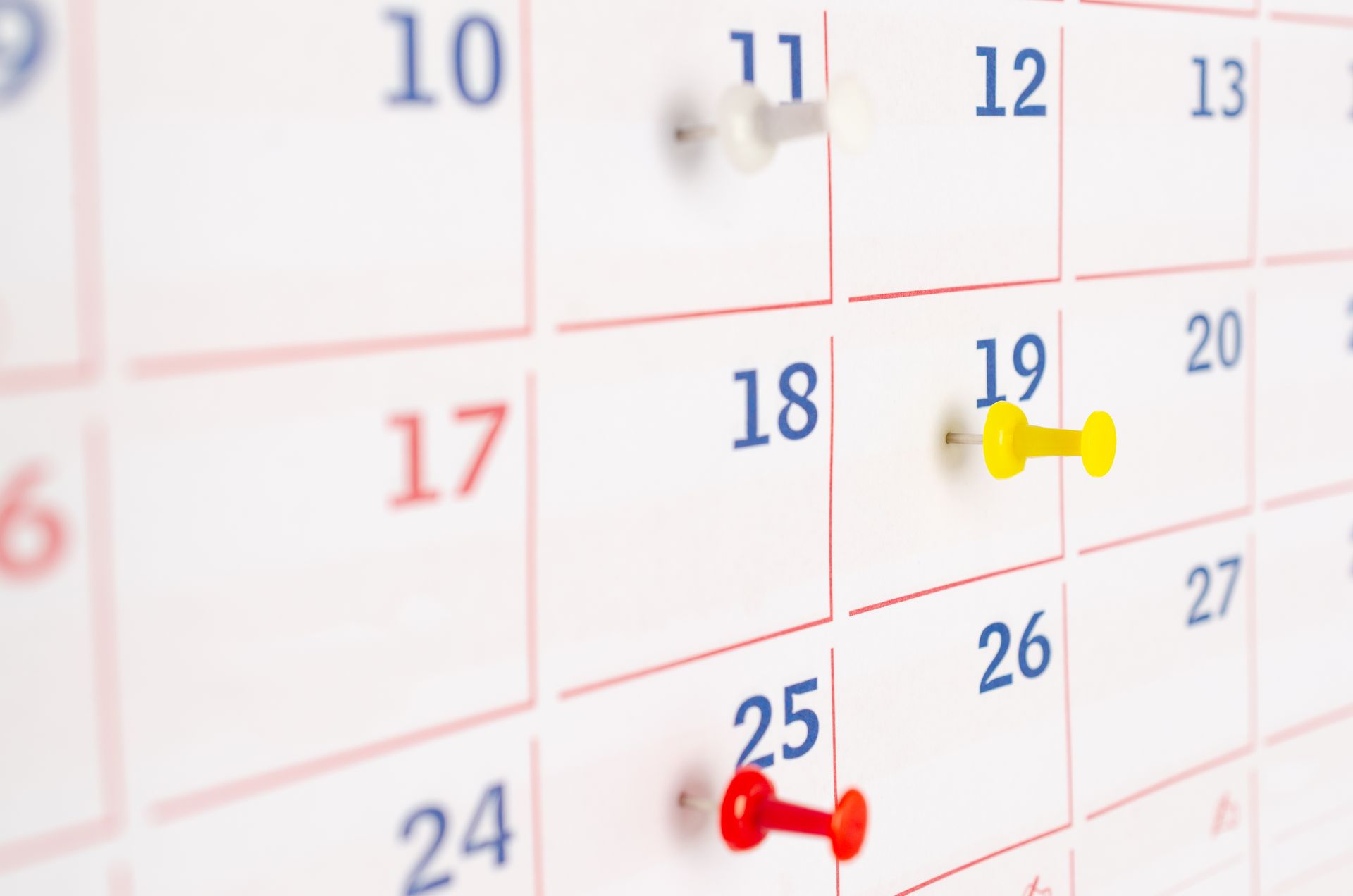 Calendar close-up with blue, yellow, and red pushpins marking dates.