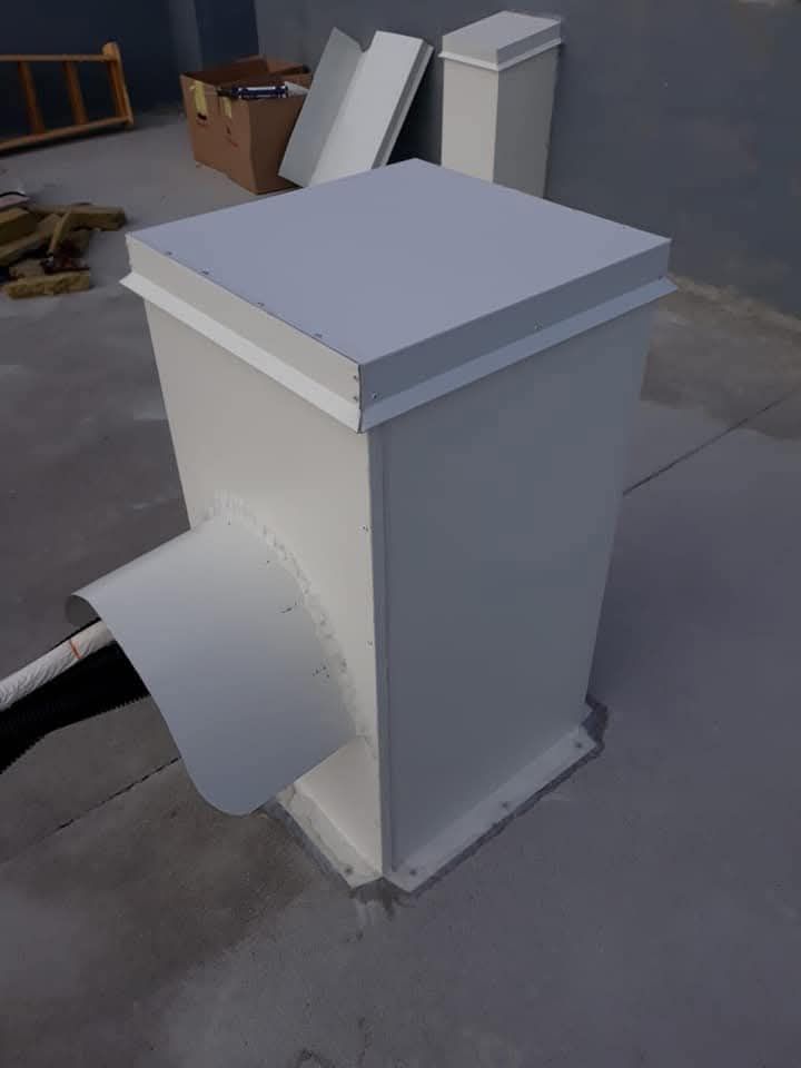 Scatola di ventilazione bianca da tetto con condotto curvo su pavimento in cemento.