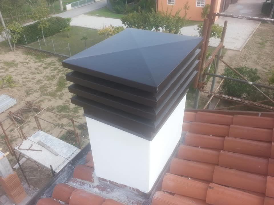 Camino sul tetto con comignolo in metallo nero e base bianca accanto a tegole rosse e un cortile recintato.