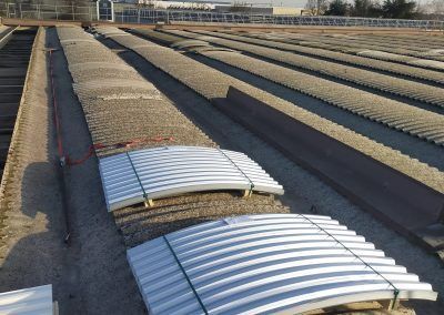 Lunghe file di pannelli ondulati argentati per tetti in un soleggiato cortile industriale.