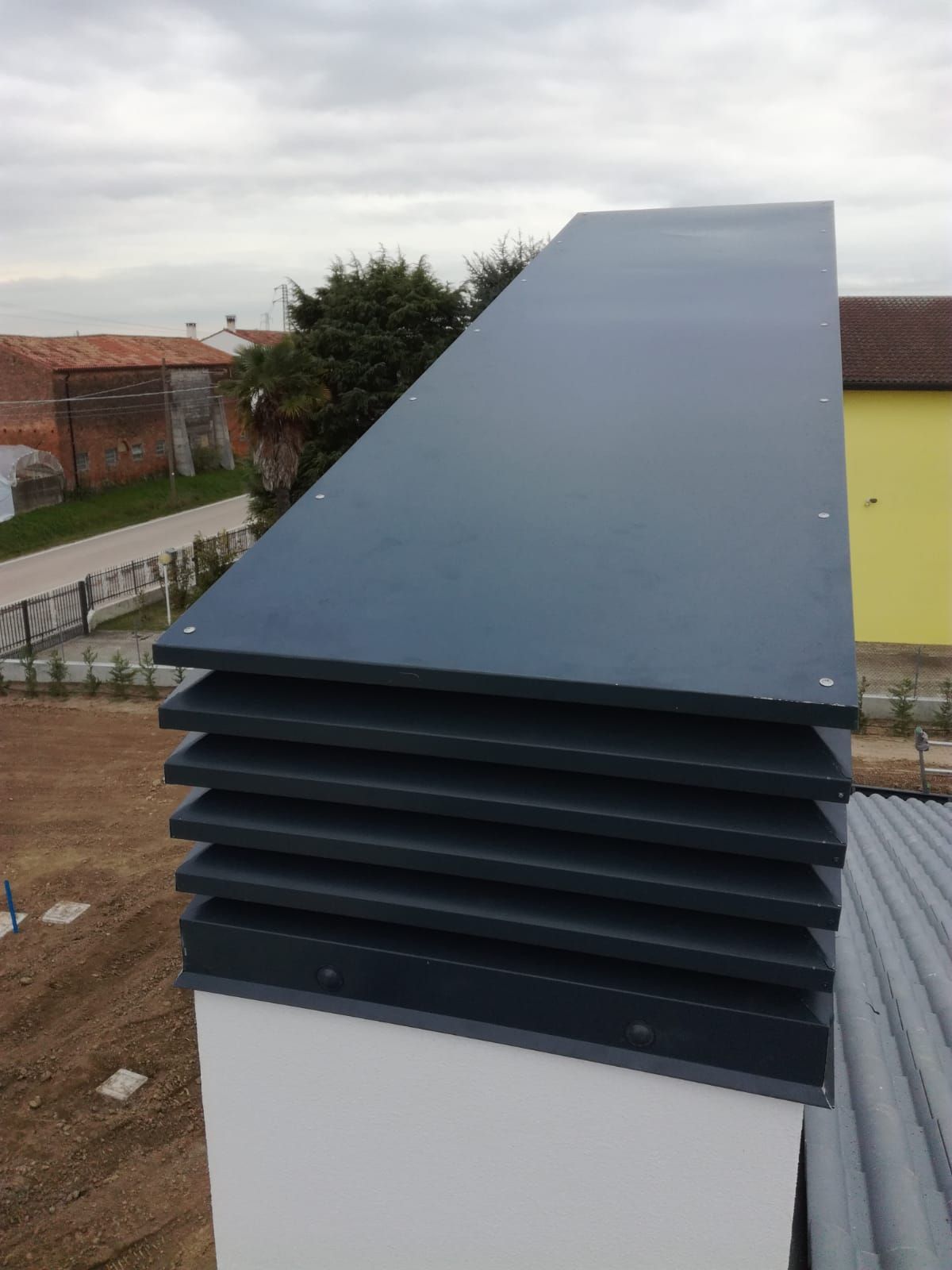 Una griglia di ventilazione grigia sul tetto di un edificio bianco, con lamelle sovrapposte.