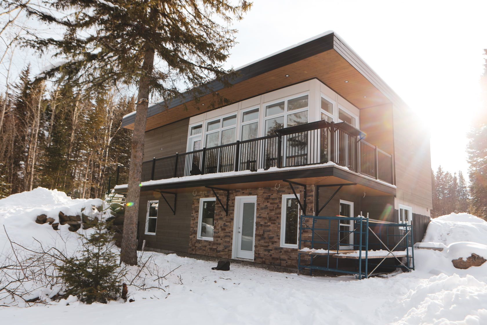 Une maison avec un balcon est entourée de neige et d'arbres.