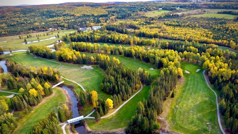 Une vue aérienne d'un terrain de golf entouré d'arbres et d'une rivière.