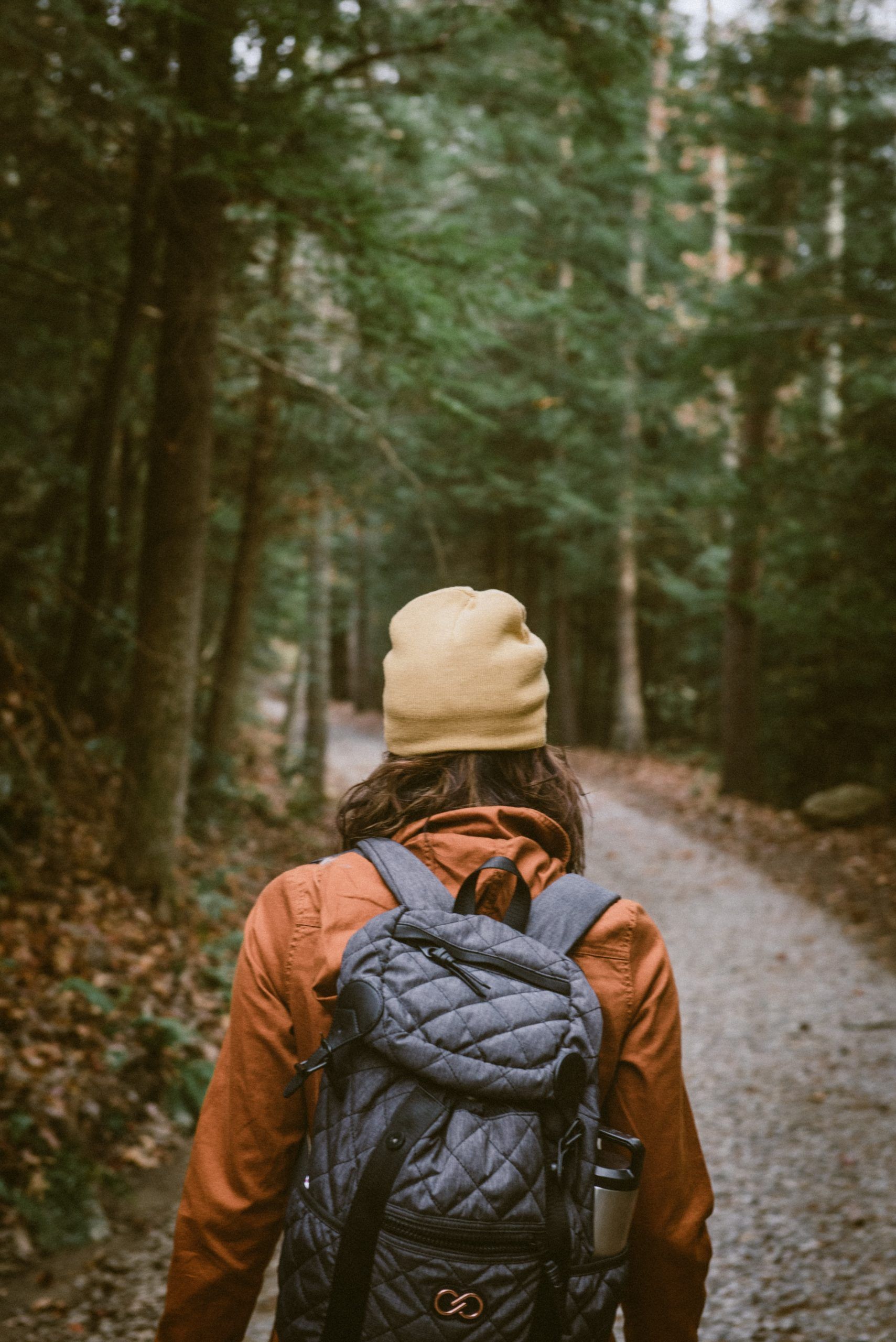 Une femme avec un sac à dos marche sur un chemin dans les bois.
