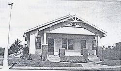 Black-and-white photo of a small house with a front porch and pitched roof.