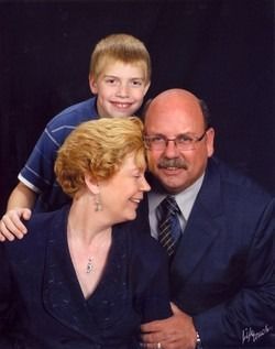 Three people posed in a studio portrait, smiling in dark formal clothing against a black backdrop.