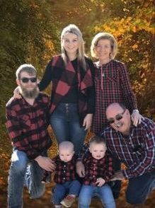 Family of five in matching red-and-black plaid shirts posed outdoors in autumn leaves