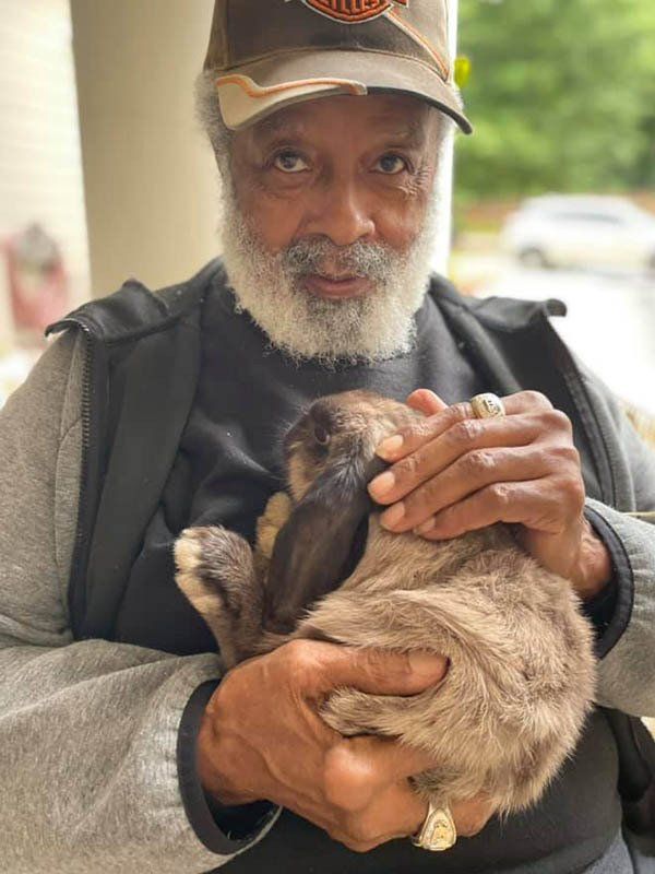 A man with a beard is holding a small rabbit in his arms.