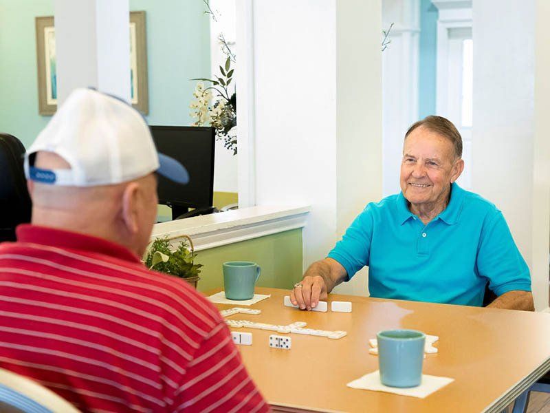 Two men are sitting at a table playing dominoes.