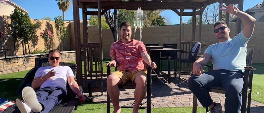 Three men relaxing outdoors while receiving IV drip therapy
