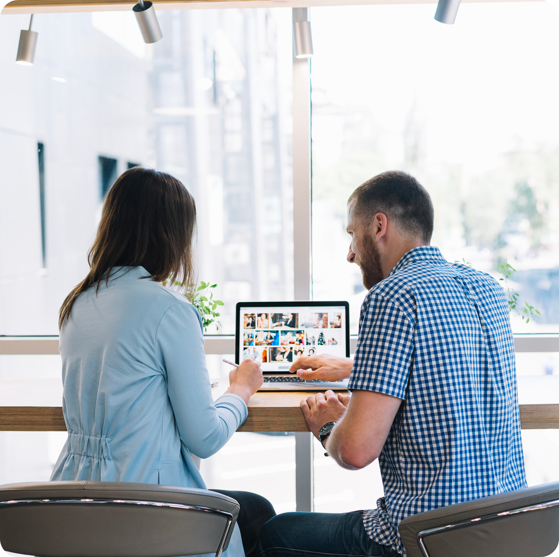 A man and a woman are sitting at a table looking at a laptop.