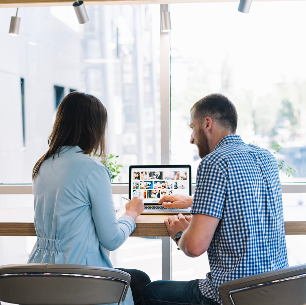 A man and a woman are sitting at a table looking at a laptop.
