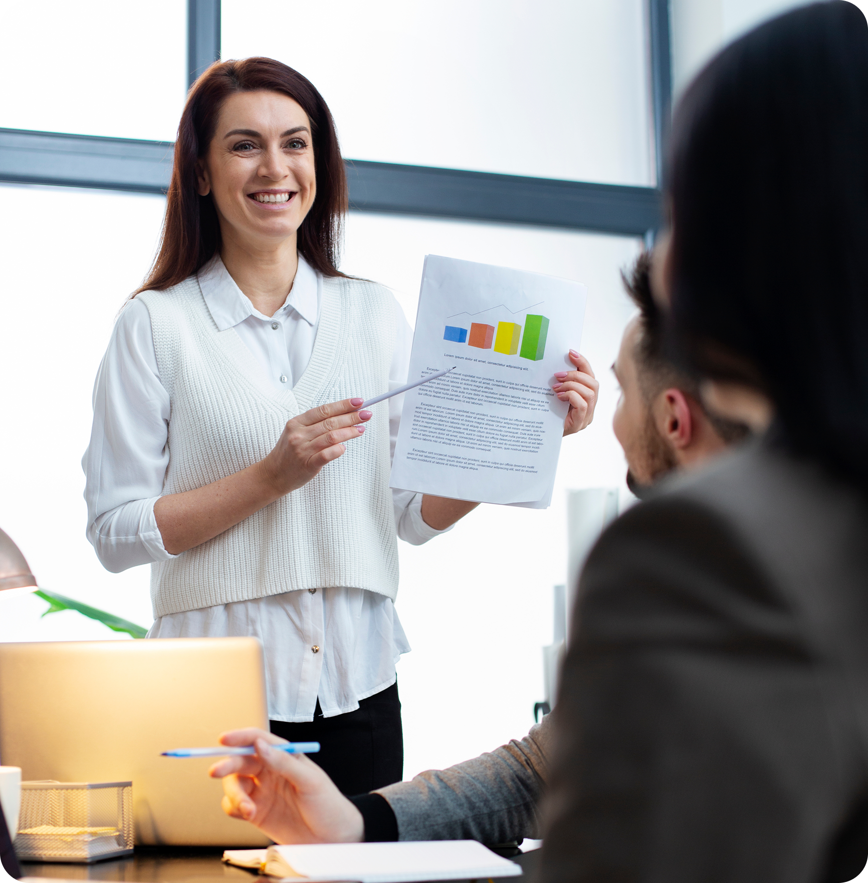 A woman is giving a presentation to a group of people while holding a piece of paper with a graph on it.