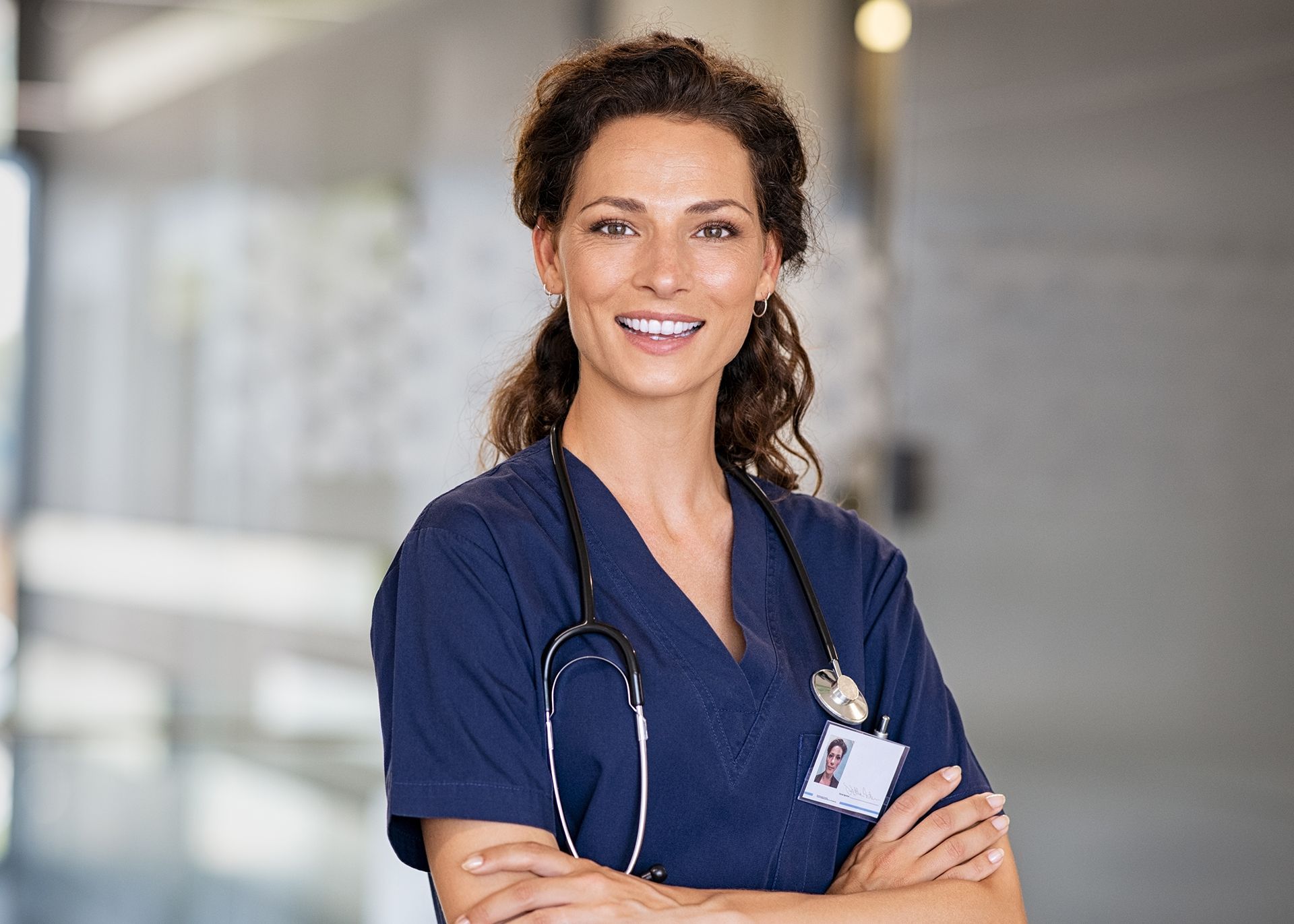 Smiling nurse in blue scrubs with stethoscope standing in hospital corridor