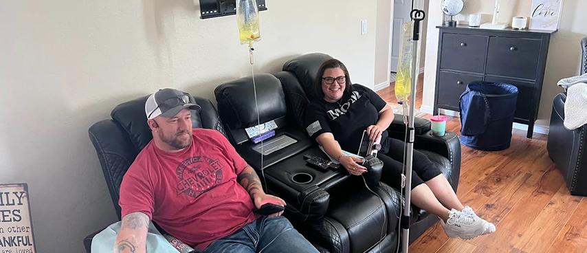 Man and woman receiving in-home IV drip therapy on reclining sofa