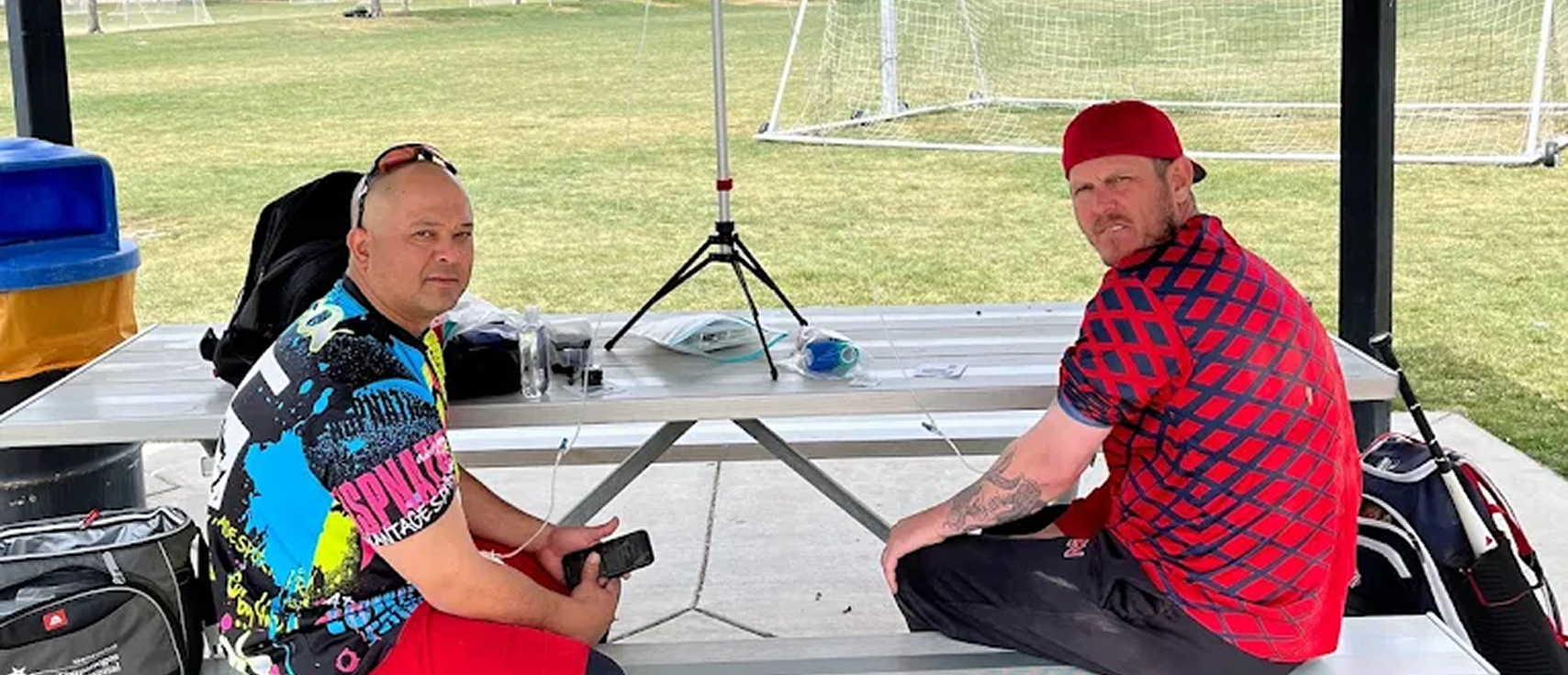 Two men receiving IV hydration therapy at outdoor park picnic table