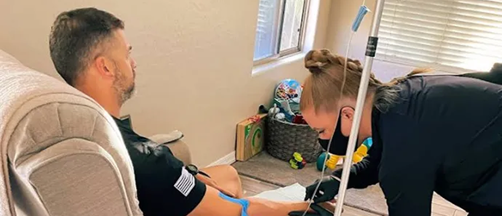 Nurse administering at-home IV drip therapy to man sitting in armchair