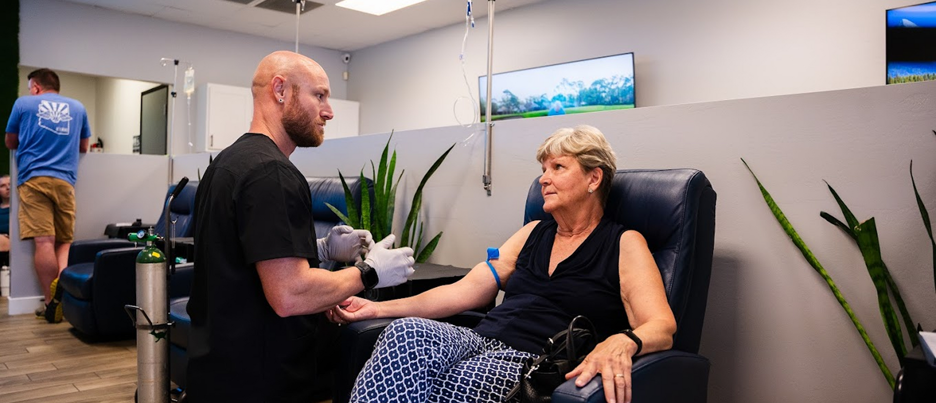 Nurse talking to senior woman receiving IV therapy in clinic recliner