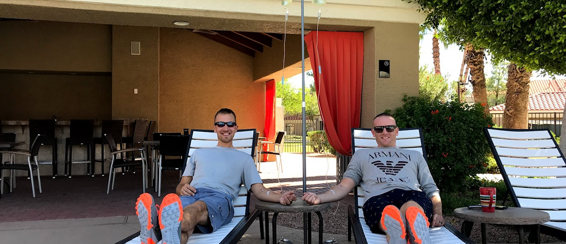 Two men receiving IV drip therapy while relaxing on outdoor lounge chairs
