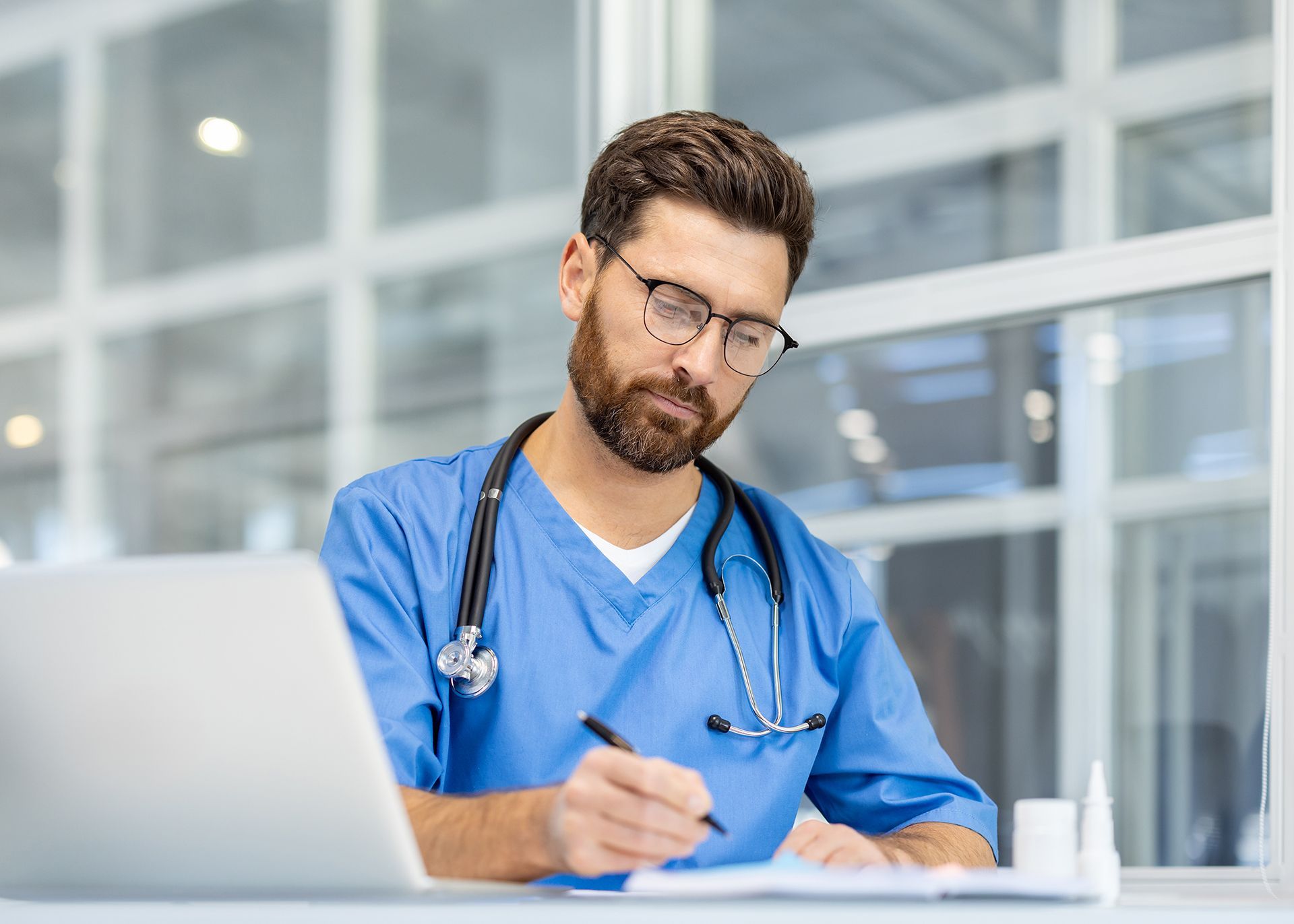 Medical director in blue scrubs reviewing documentation at a desk for mobile IV therapy compliance