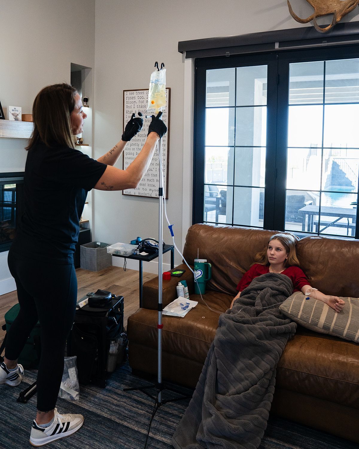 Nurse adjusting IV bag while patient rests on couch at home