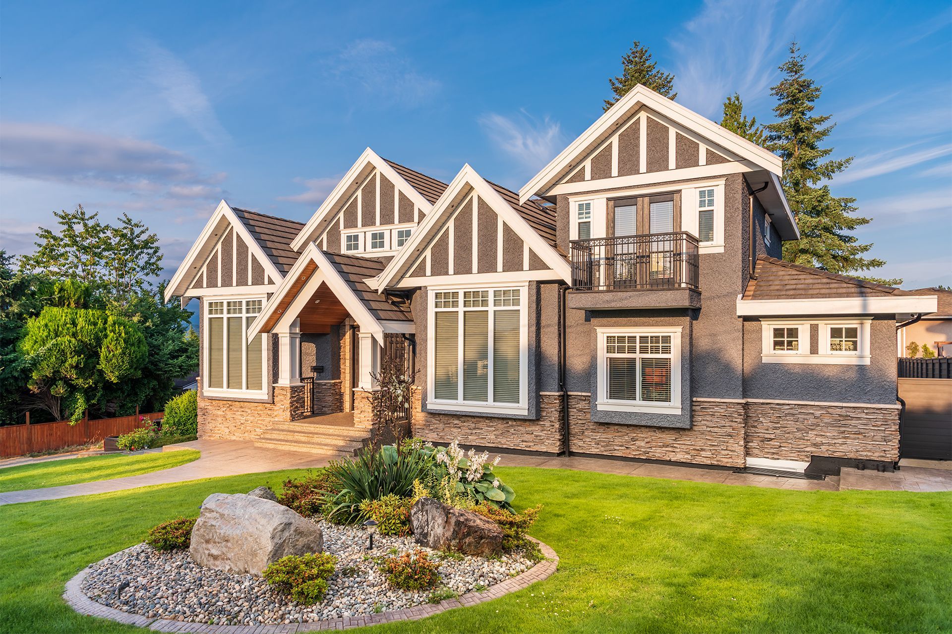 Large modern suburban house with stone and white trim, a landscaped lawn, and blue sky.