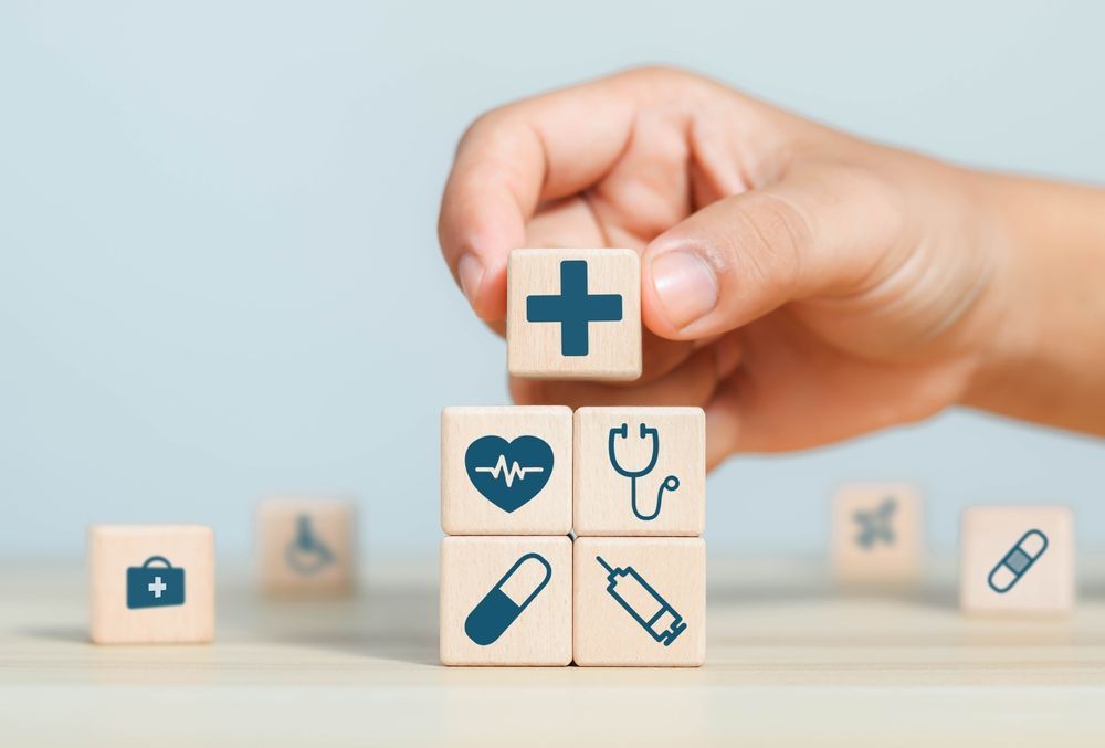 Hand placing a medical cross cube on stacked health-care blocks with icons on a light background